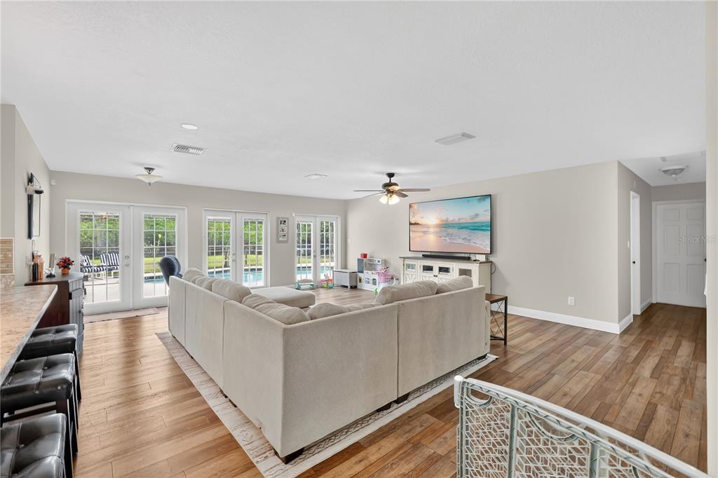 A living room features wood-look flooring, a large sectional sofa, and glass doors to a pool — 1985 MUSTANG COURT, ST CLOUD, FL