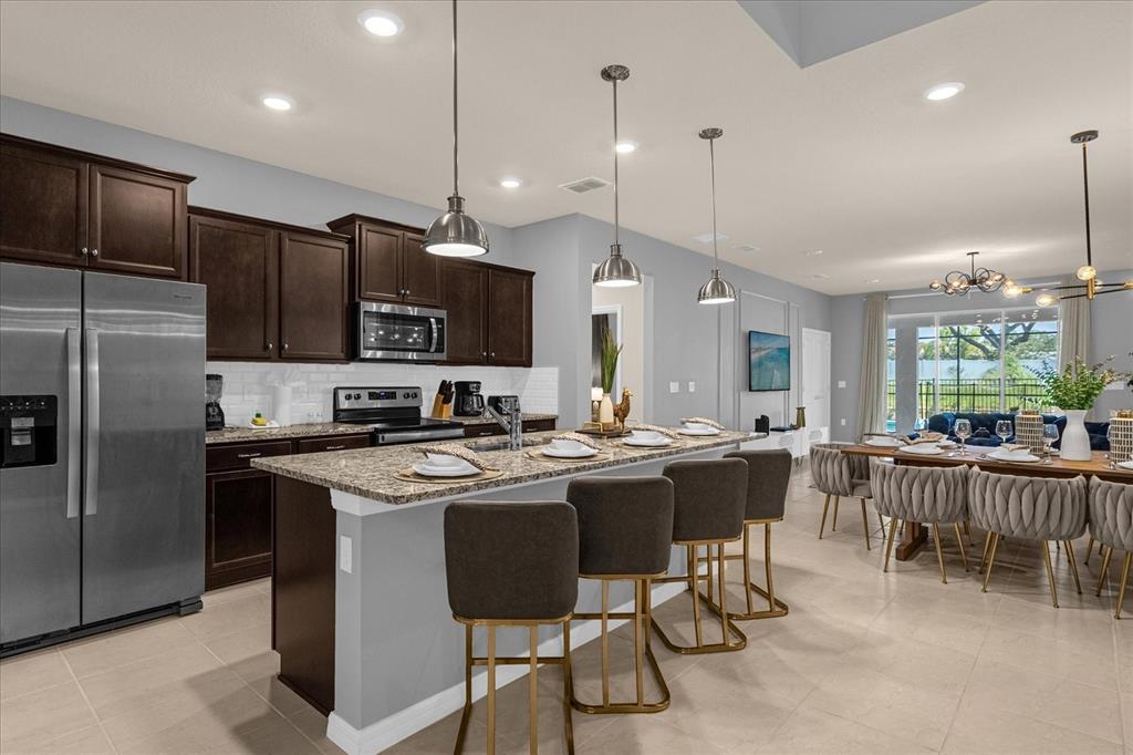 A kitchen with dark wood cabinets, granite countertops, and an island with four bar stools — 3937 LANA AVENUE, DAVENPORT, FL