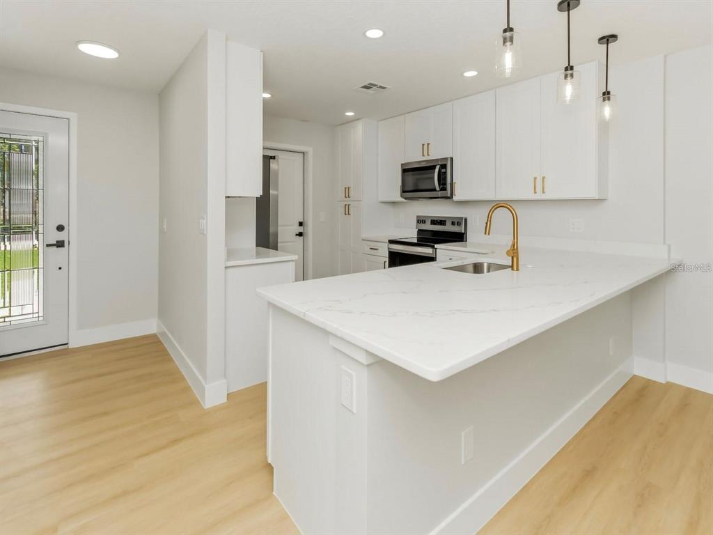 A modern kitchen features white cabinets, a quartz island, and light wood-look flooring — 3058 GRACELAND COURT, ORLANDO, FL