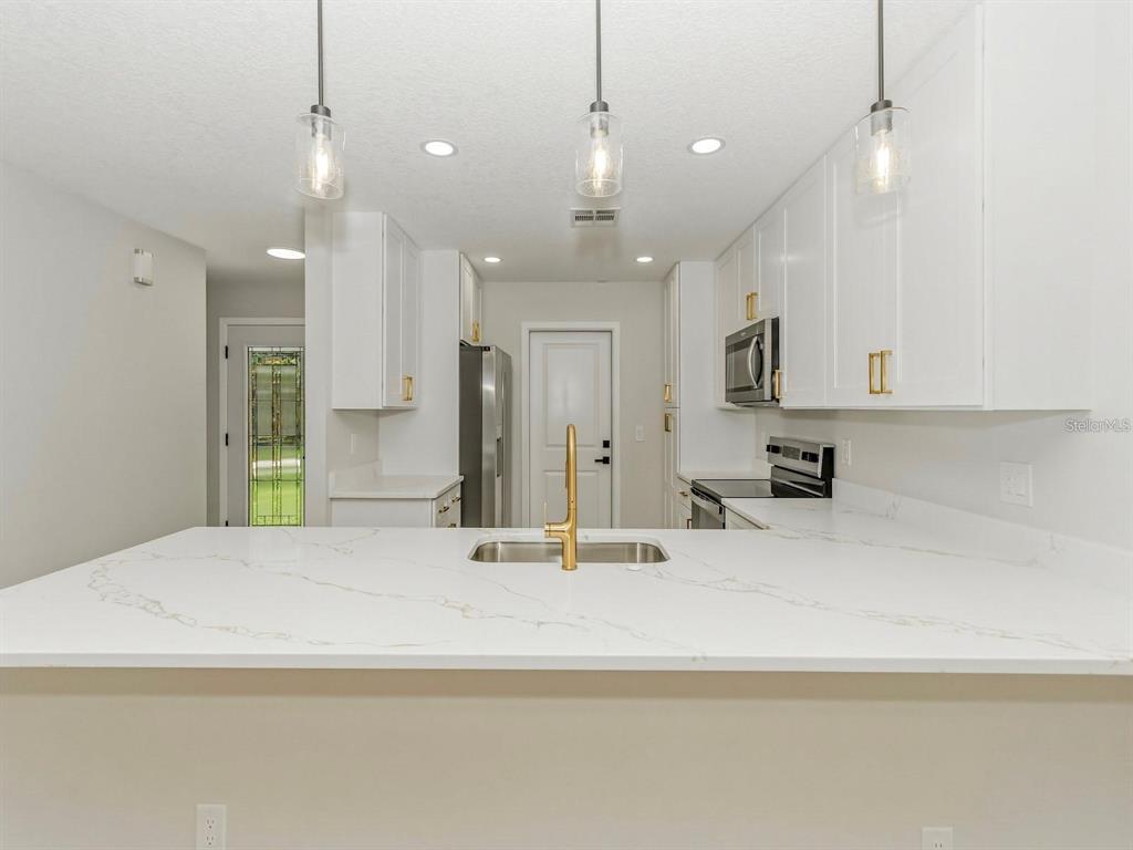 A modern kitchen features white cabinets, a marble-look countertop, and a gold faucet — 3058 GRACELAND COURT, ORLANDO, FL