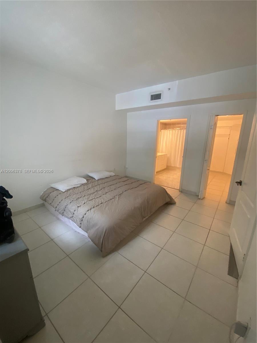 A bedroom features a bed, tiled floors, and doorways leading to a bathroom and closet — 17405 NW 75th Pl # 107, Hialeah FL 33015, HIALEAH, FL
