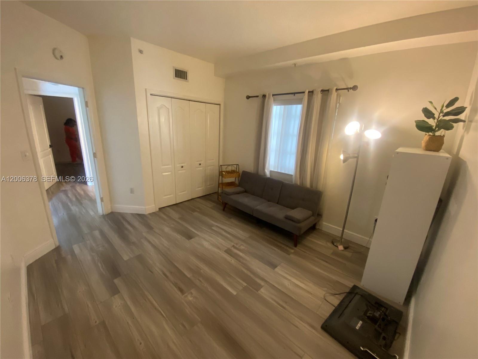 A room with wood-look flooring, a grey sofa, a floor lamp, and a closet — 17405 NW 75th Pl # 107, Hialeah FL 33015, HIALEAH, FL