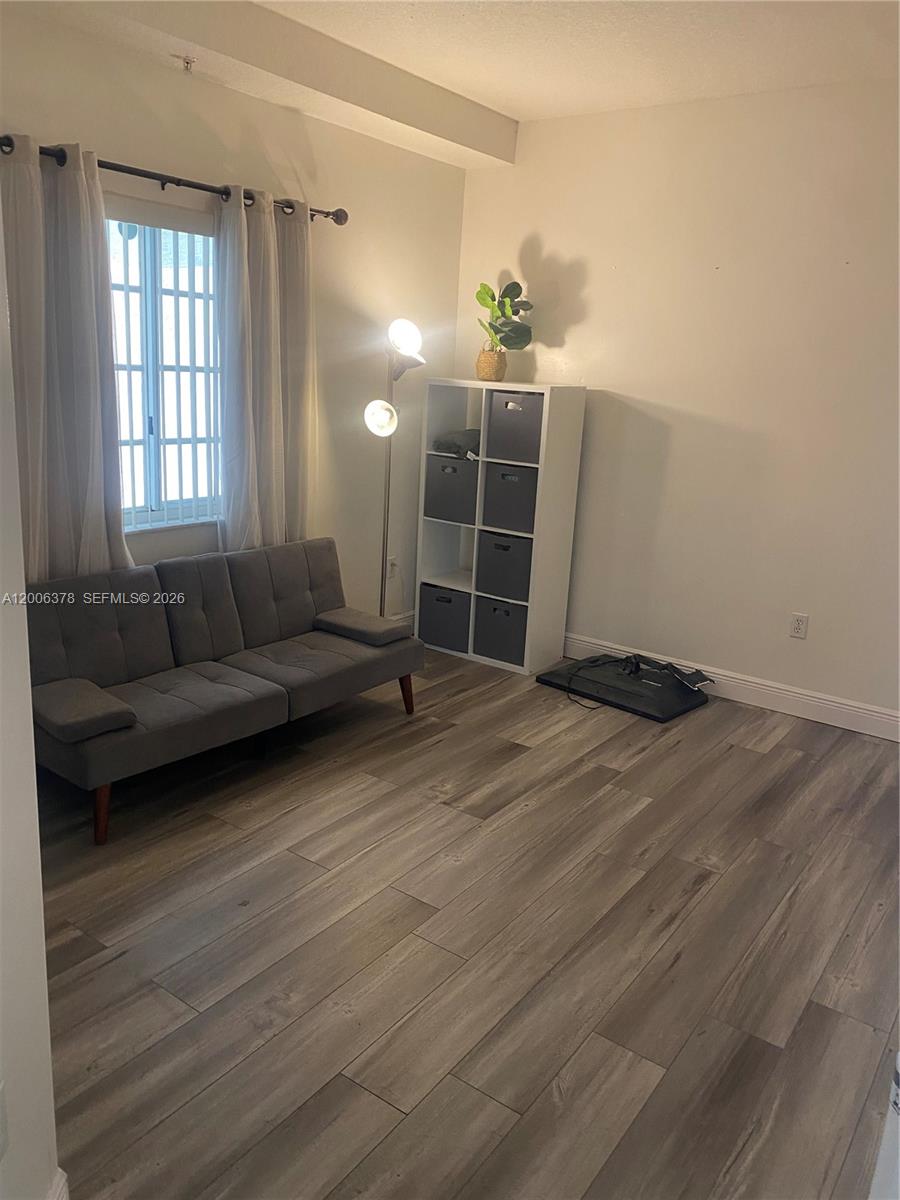 A room with wood-look flooring, a gray futon, a floor lamp, and a storage unit — 17405 NW 75th Pl # 107, Hialeah FL 33015, HIALEAH, FL