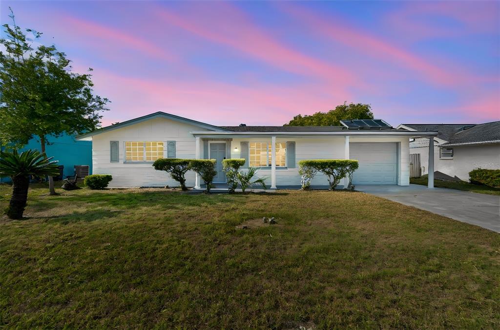 A single-story white house with a garage and solar panels sits under a sunset sky — 3667 ROCKAWAY DRIVE, HOLIDAY, FL