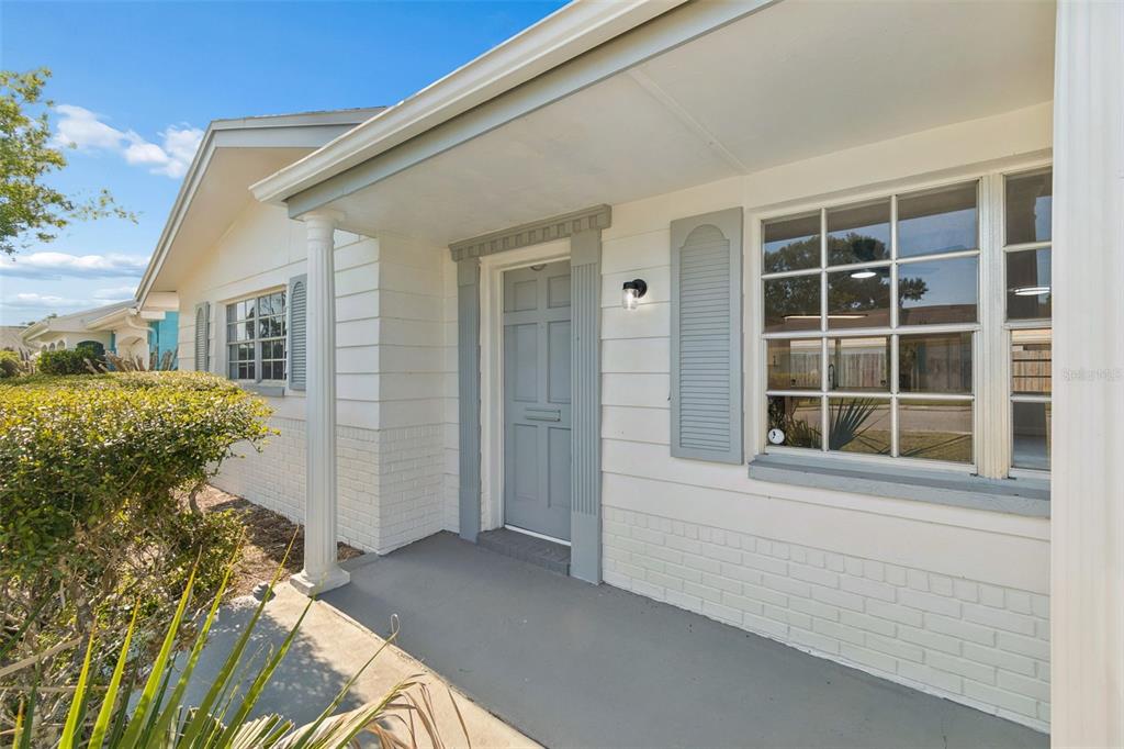 A gray front door with matching shutters on a white brick house with a porch — 3667 ROCKAWAY DRIVE, HOLIDAY, FL