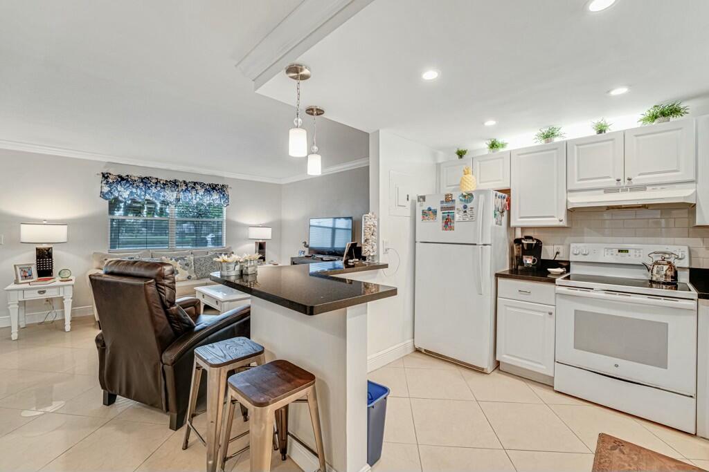 A kitchen with white cabinets and a breakfast bar overlooks a living room area — 350 Tuscany G, Delray Beach FL 33446, DELRAY BEACH, FL