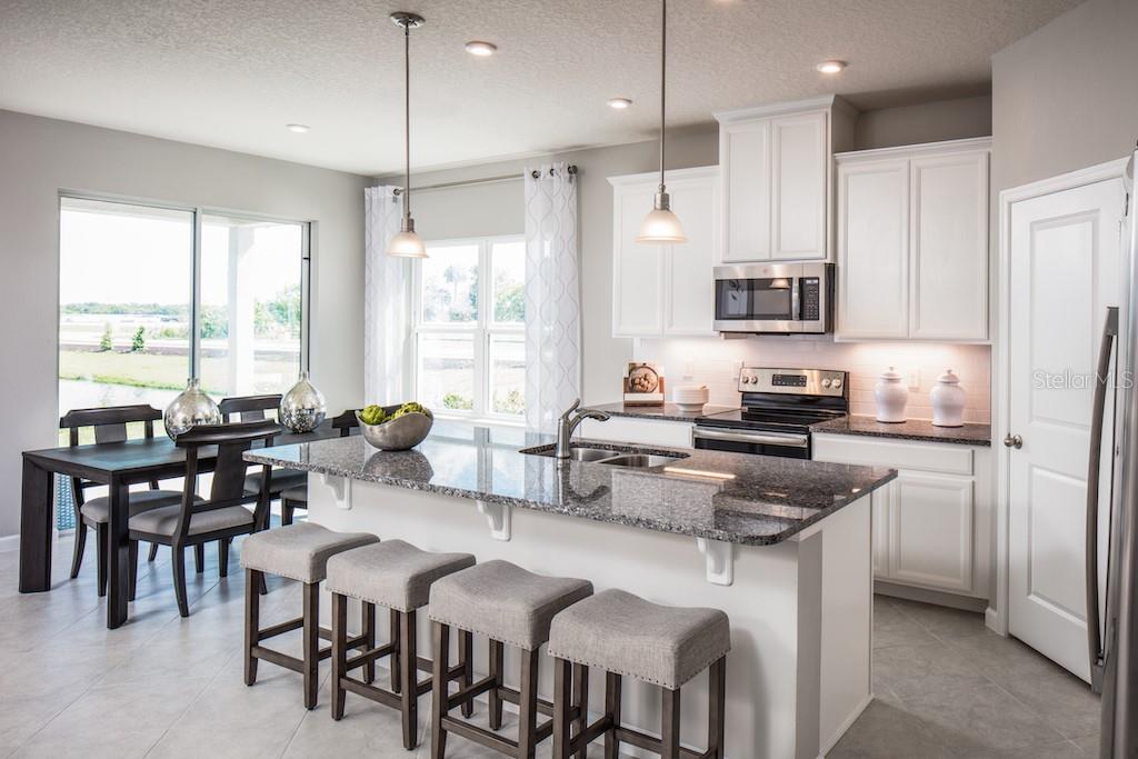 A kitchen with white cabinets, granite countertops, a center island with bar stools, and dining area — 1100 OCEAN LODGE ROAD, LADY LAKE, FL
