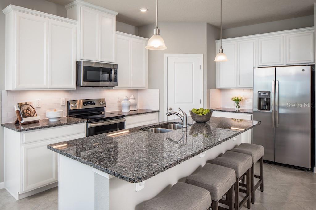 A kitchen features white cabinets, granite countertops, a center island with seating, and stainless appliances — 1100 OCEAN LODGE ROAD, LADY LAKE, FL