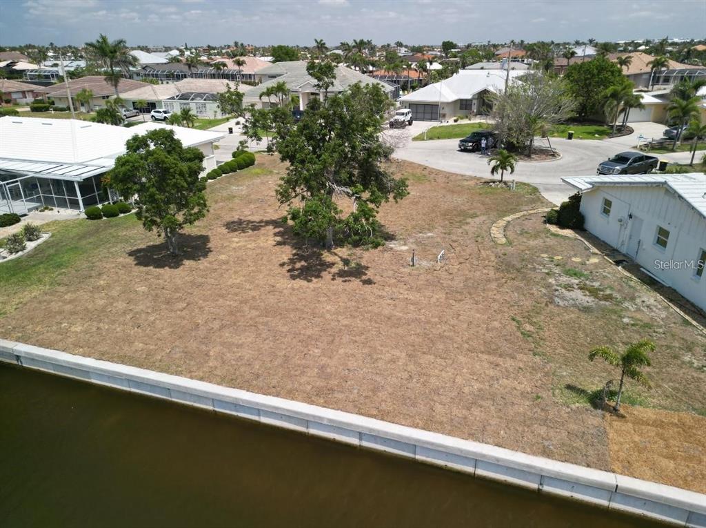 An aerial view shows a vacant waterfront lot with two large trees and surrounding houses — 571 BELVEDERE COURT, PUNTA GORDA, FL