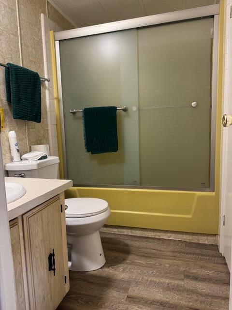 A bathroom features a yellow tub surround, sliding glass doors, a toilet, and wood-look flooring — 1065 Echo Avenue, Moore Haven FL 33471, MOORE HAVEN, FL
