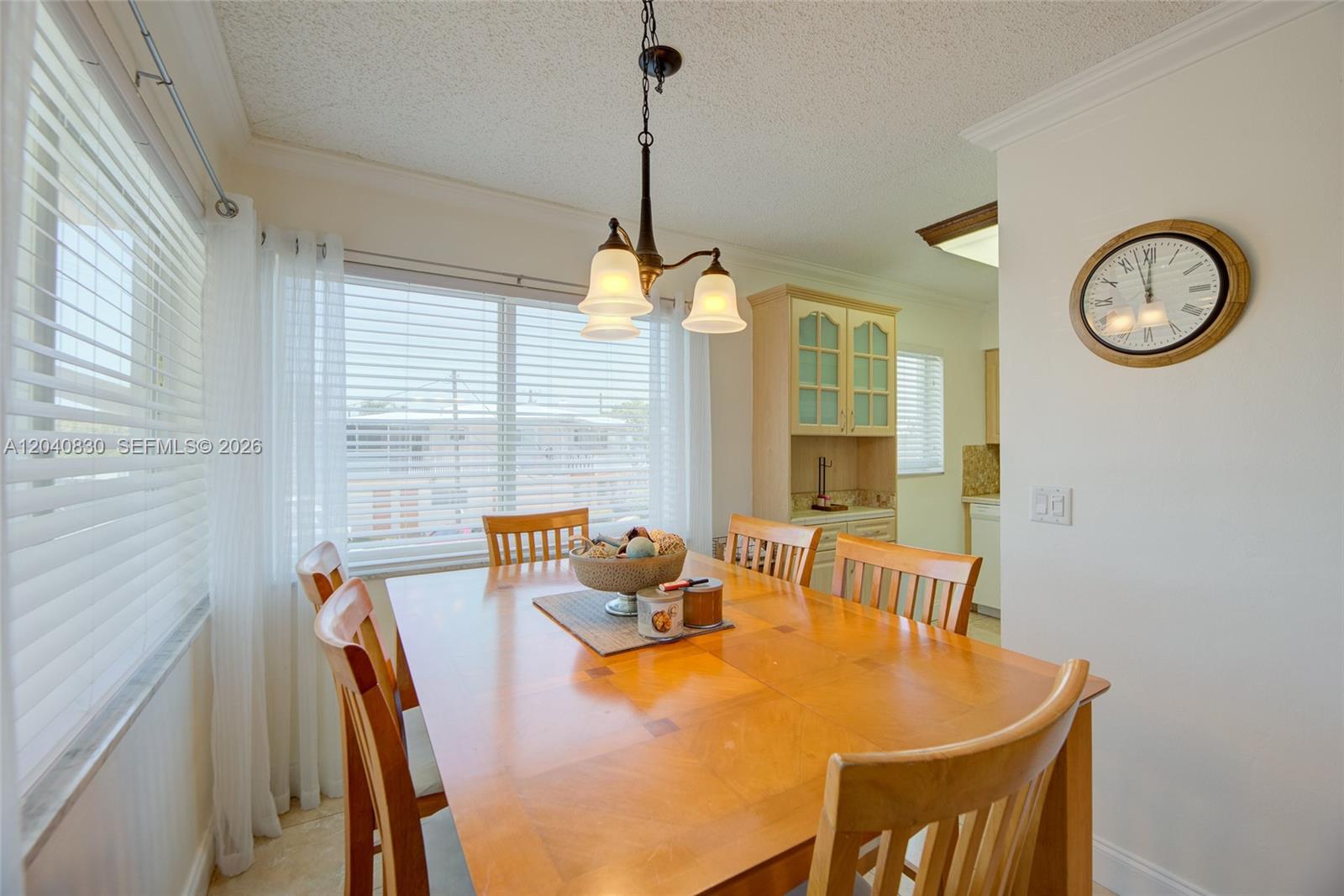 A dining room features a wooden table, six chairs, a hanging light fixture, and a clock — 920 SW 10th Ter # 12R, Hallandale Beach FL 33009, HALLANDALE BEACH, FL