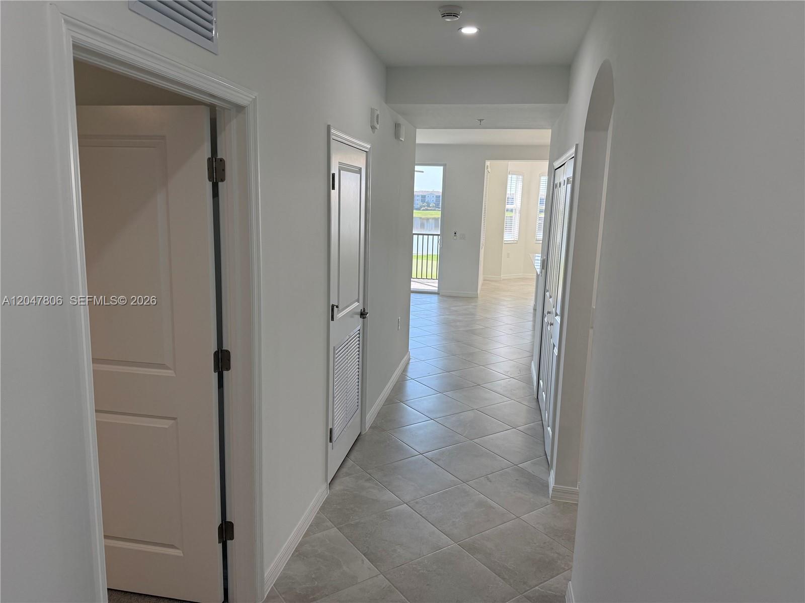 A hallway with light-colored tile flooring leads toward a bright living area with a balcony — 5491 Double Eagle Cir # 3732, Ave Maria FL 34142, AVE MARIA, FL