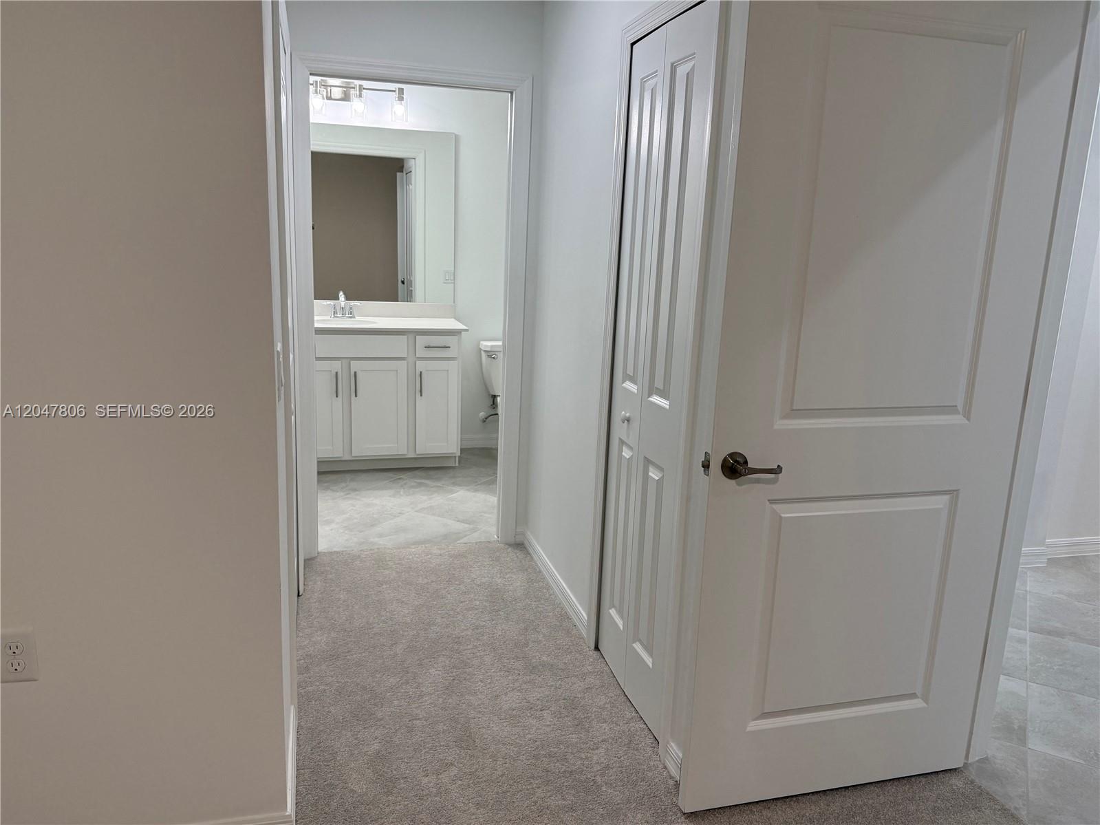 A hallway with carpeted flooring leads to a bathroom with a white vanity and mirror — 5491 Double Eagle Cir # 3732, Ave Maria FL 34142, AVE MARIA, FL