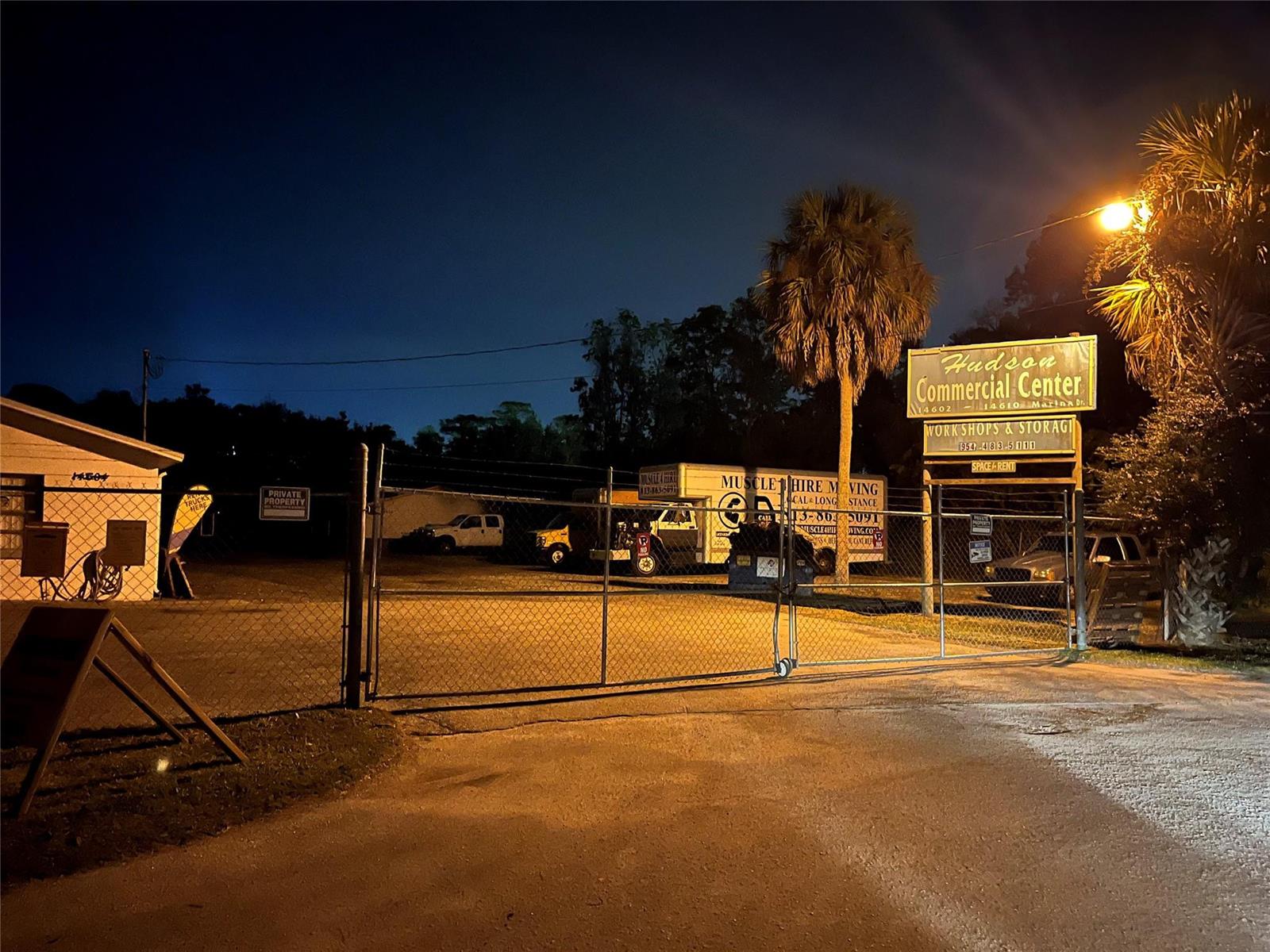 A gated commercial storage facility at night with a sign and parked moving trucks — 14600 Marina Drive, FL 34667, FL