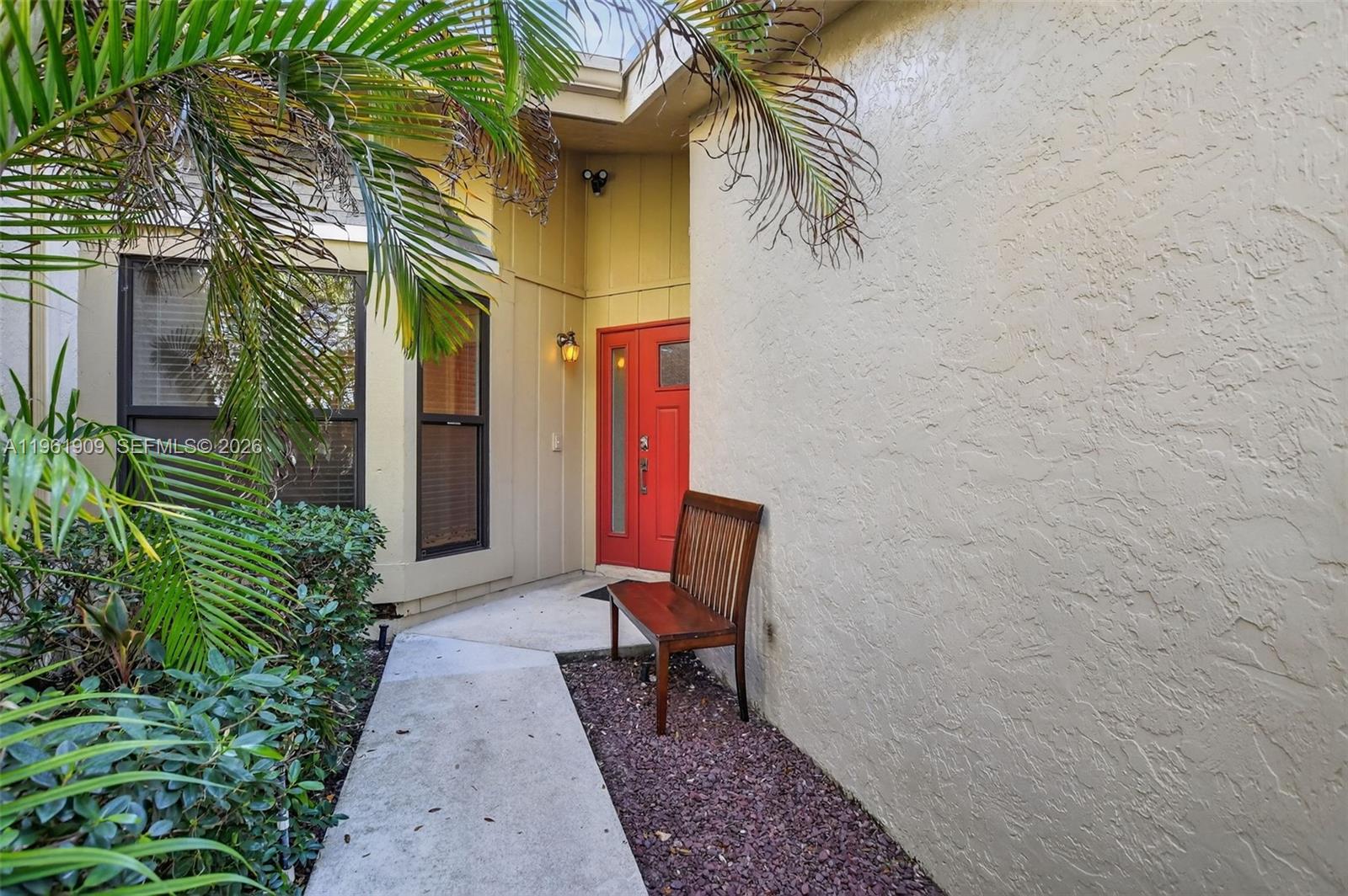 A red front door is situated at the end of a concrete walkway with a bench — 1400 NW 9th Ave # 2, Boca Raton FL 33486, BOCA RATON, FL