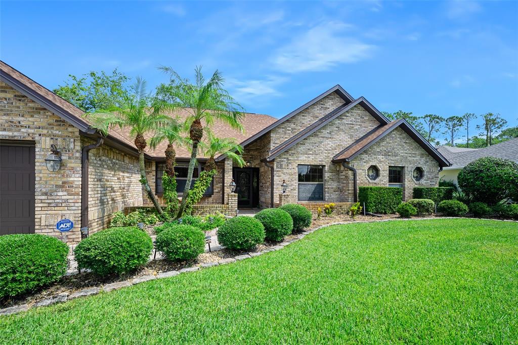 A brick house with a manicured lawn, palm trees, and a dark-colored front door — 43 WINDING CREEK WAY, ORMOND BEACH, FL