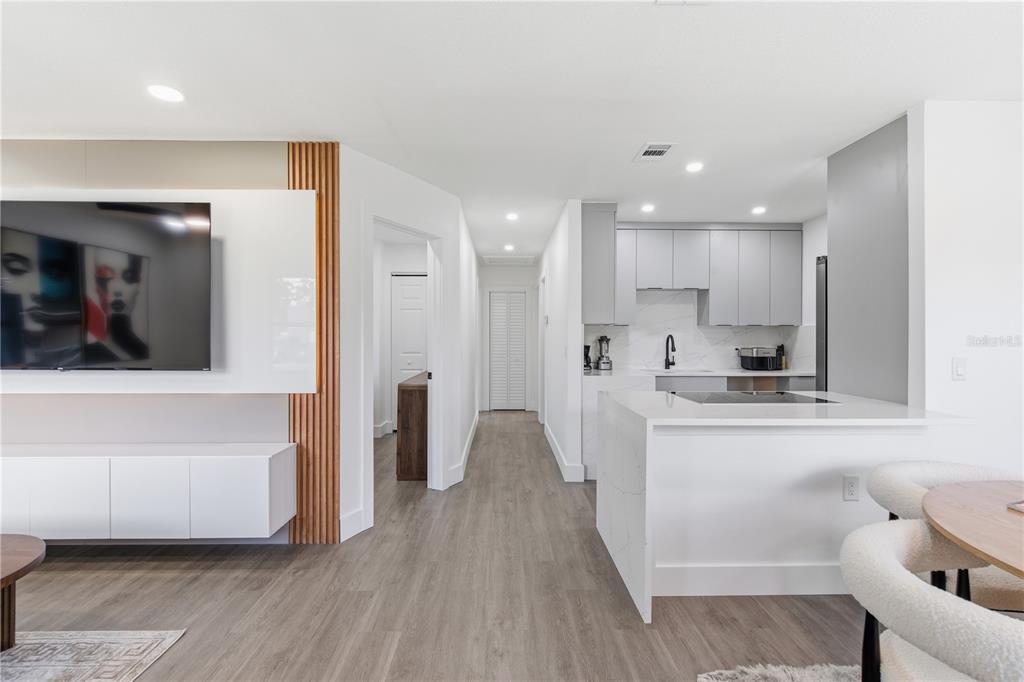 A modern open-concept living area features a white media wall, wood slats, and a kitchen — 6713 S MASCOTTE STREET, TAMPA, FL