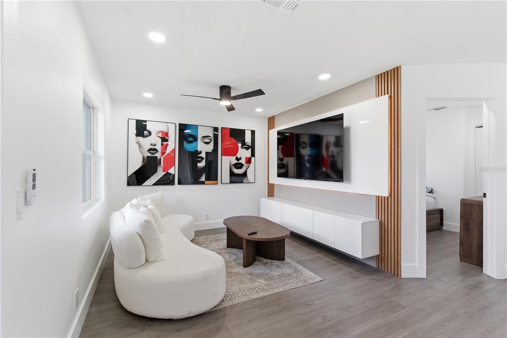A modern living room features a curved white sofa, wall art, and a wall-mounted television — 6713 S MASCOTTE STREET, TAMPA, FL