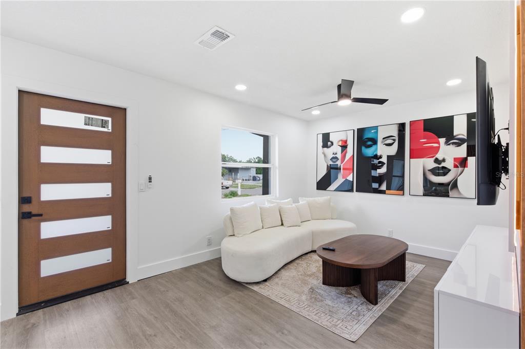 A modern living room features a curved white sofa, wood coffee table, and pop-art wall decor — 6713 S MASCOTTE STREET, TAMPA, FL