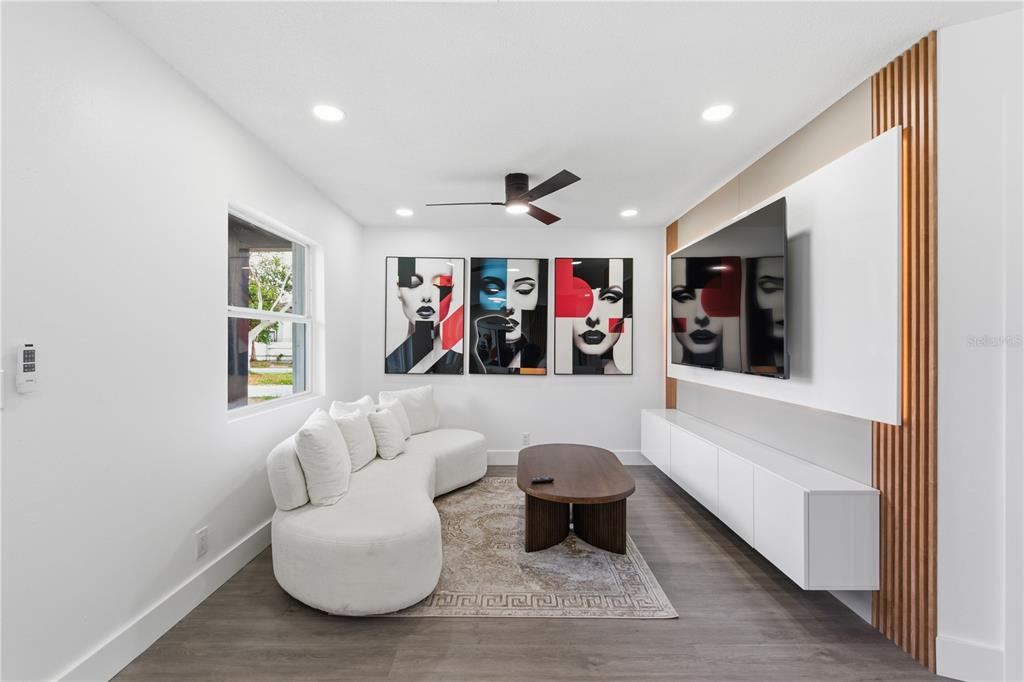A modern living room features a curved white sofa, wall art, and a wall-mounted television — 6713 S MASCOTTE STREET, TAMPA, FL