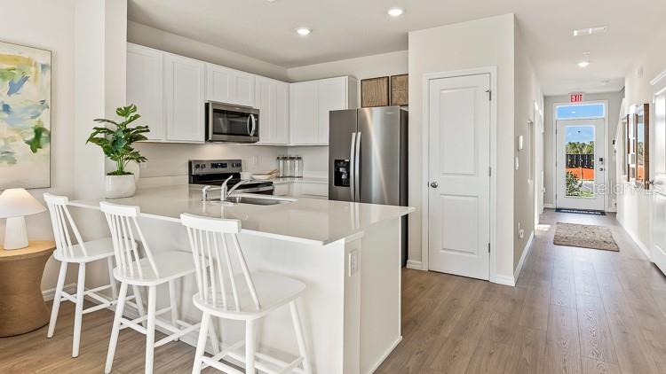 A modern kitchen features white cabinetry, stainless steel appliances, and a breakfast bar with stools — 18655 BUCKSKIN DRIVE, LAKEWOOD RANCH, FL