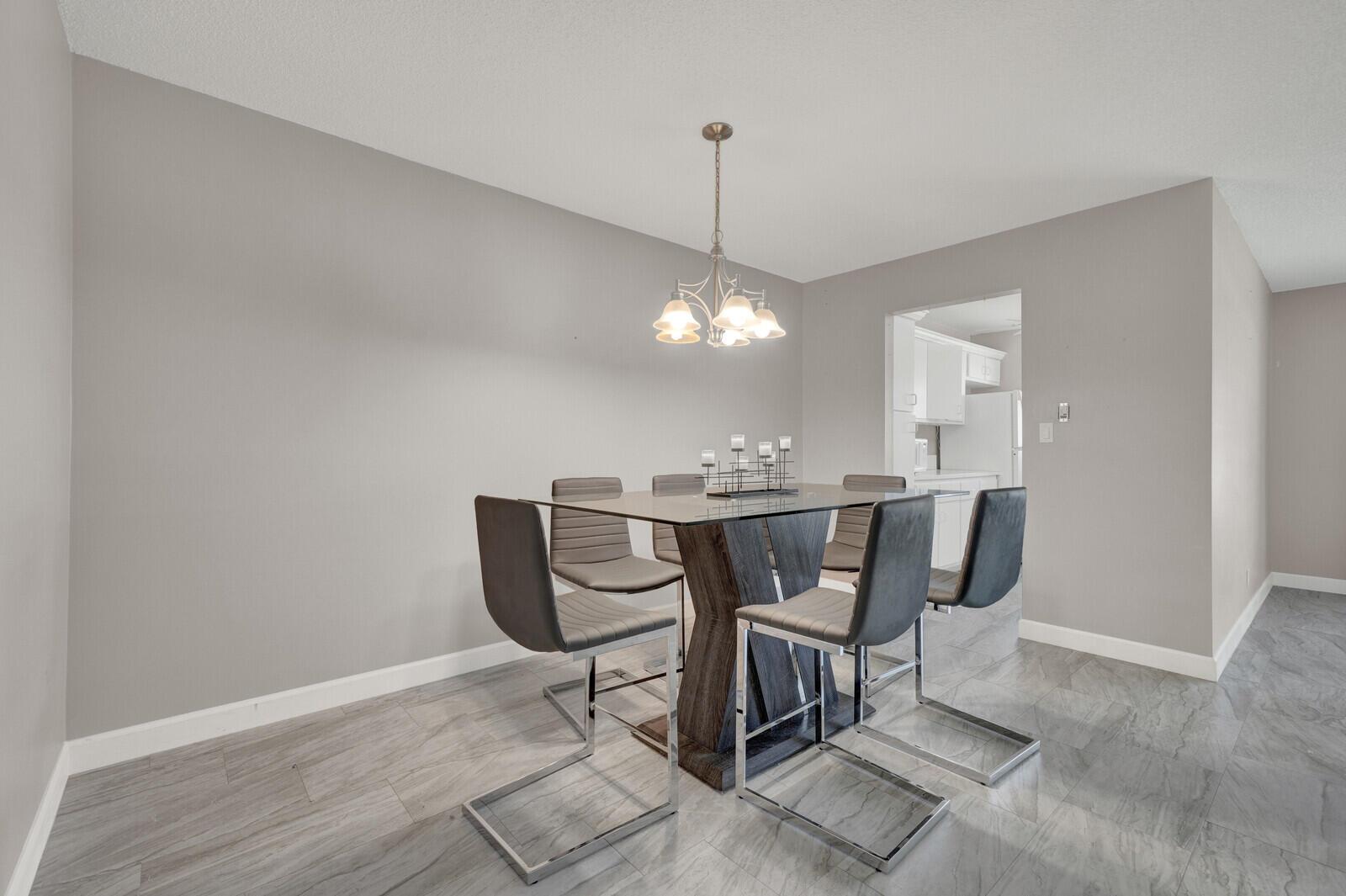 A dining room features a glass-topped table, six modern chairs, and gray tile flooring — 185 High Point Terrace E # B, Delray Beach FL 33445, DELRAY BEACH, FL
