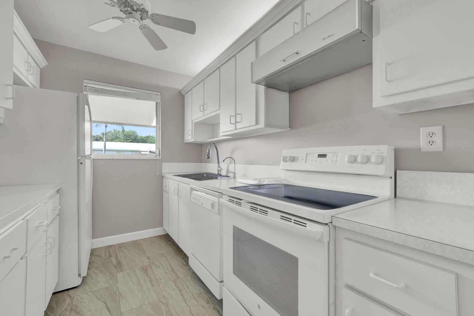 A white kitchen features white cabinets, a white stove, a dishwasher, and light-colored tile flooring — 185 High Point Terrace E # B, Delray Beach FL 33445, DELRAY BEACH, FL