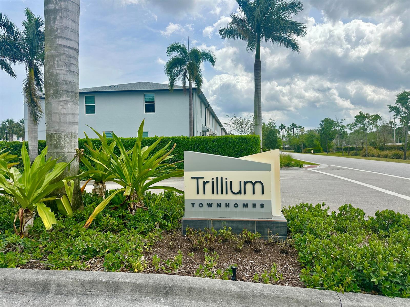 A sign for Trillium Townhomes stands in a landscaped area with palm trees and buildings — 2401 SE Tarvest Way, Stuart FL 34997, STUART, FL