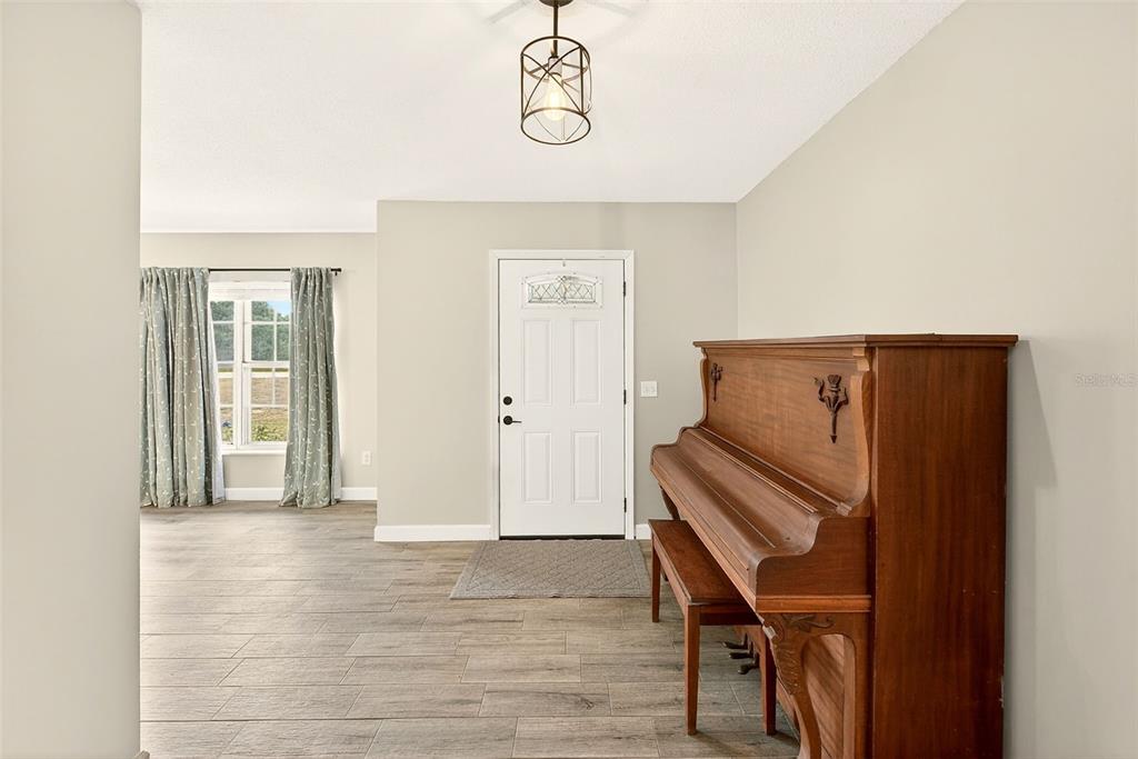 An entryway features wood-look tile flooring, a white front door, and an upright wooden piano — 1017 CAROLINA AVENUE, MULBERRY, FL