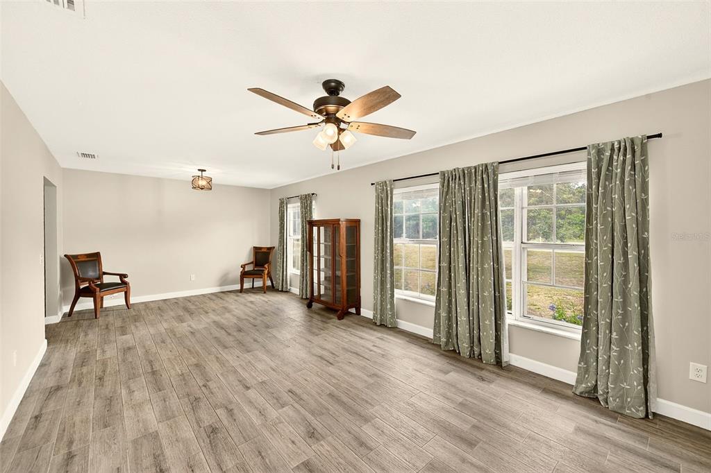 A spacious room features light wood-look flooring, a ceiling fan, and large windows with curtains — 1017 CAROLINA AVENUE, MULBERRY, FL