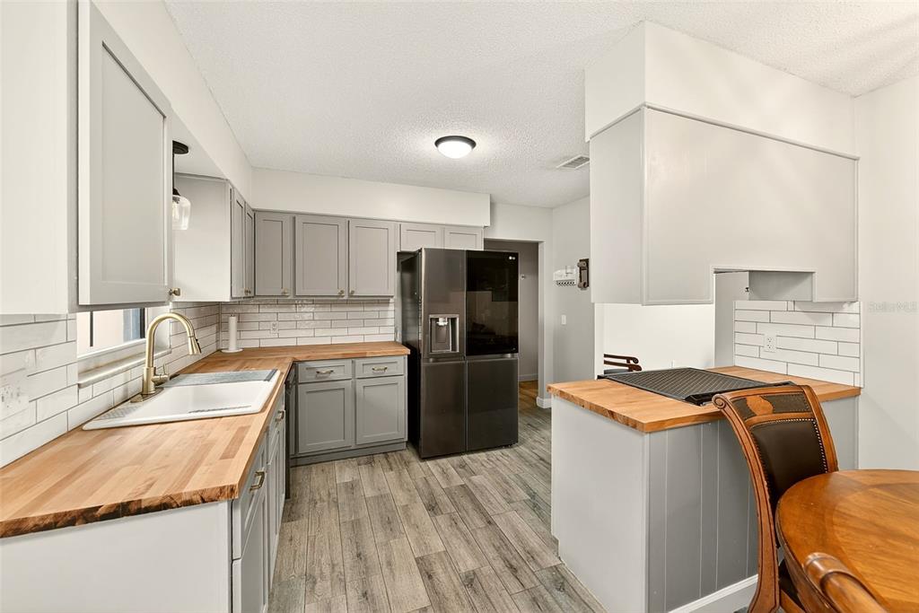 A kitchen features gray cabinets, butcher block countertops, a white farmhouse sink, and wood-look flooring — 1017 CAROLINA AVENUE, MULBERRY, FL