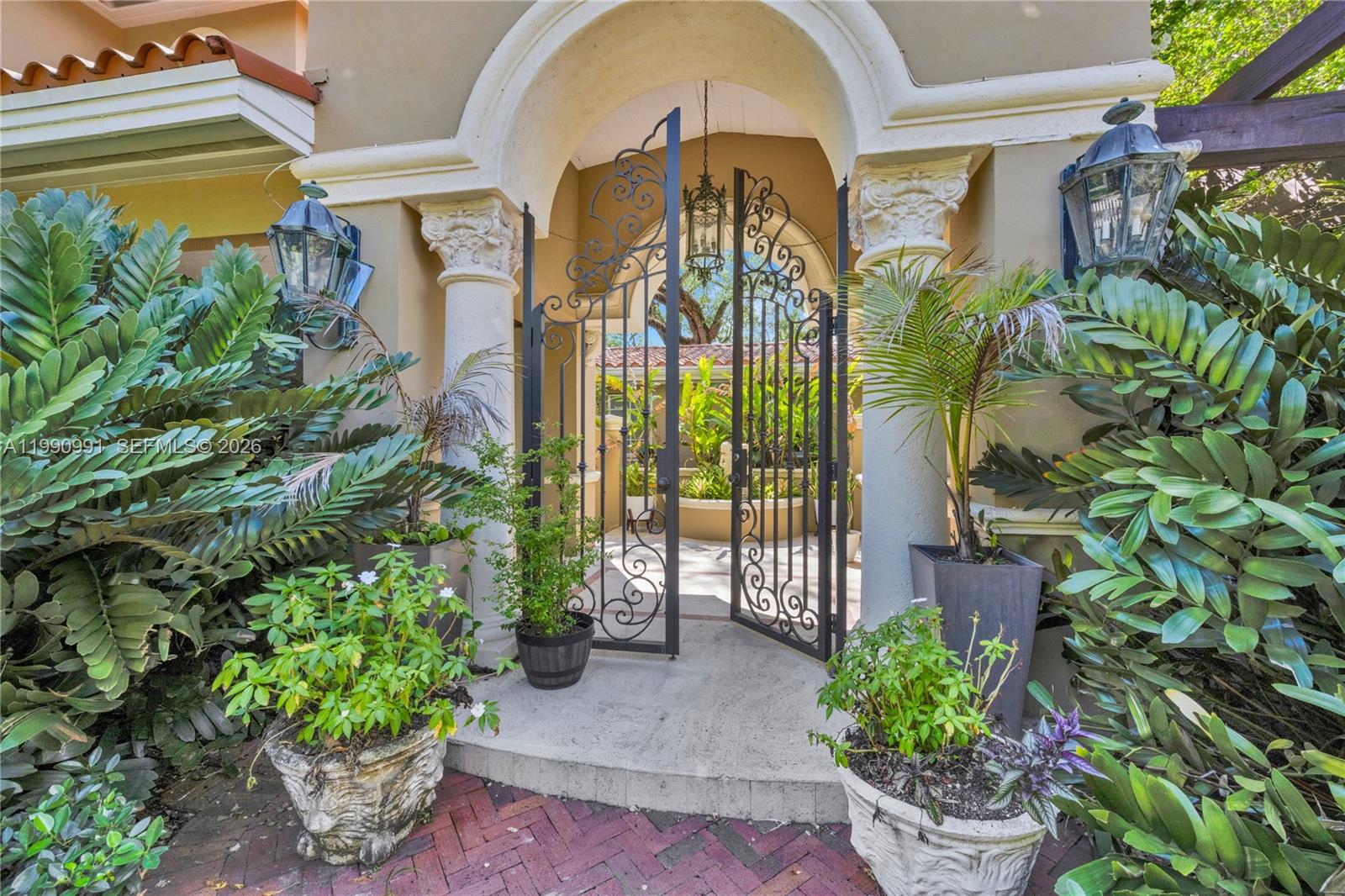 An arched entryway features wrought iron gates, decorative columns, and potted plants on a brick patio — 6200 Granada Blvd, Coral Gables FL 33146, CORAL GABLES, FL