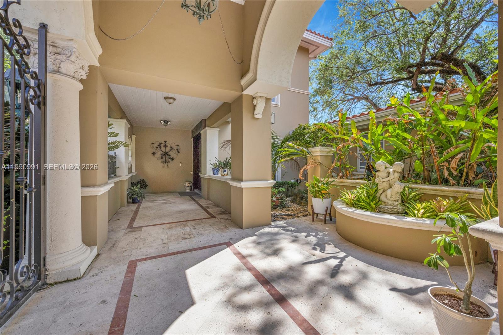A covered entryway features stone flooring, decorative columns, and a landscaped planter with a statue — 6200 Granada Blvd, Coral Gables FL 33146, CORAL GABLES, FL
