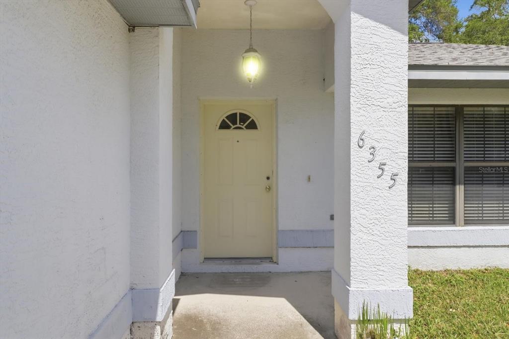 A covered front porch features a light-colored door, a hanging light, and house numbers — 6355 E RUSH STREET, INVERNESS, FL