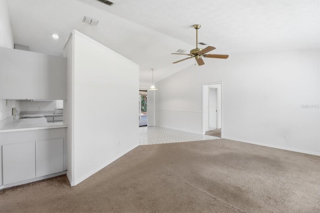 A carpeted living room opens to a kitchen and a tiled dining area with vaulted ceilings — 6355 E RUSH STREET, INVERNESS, FL