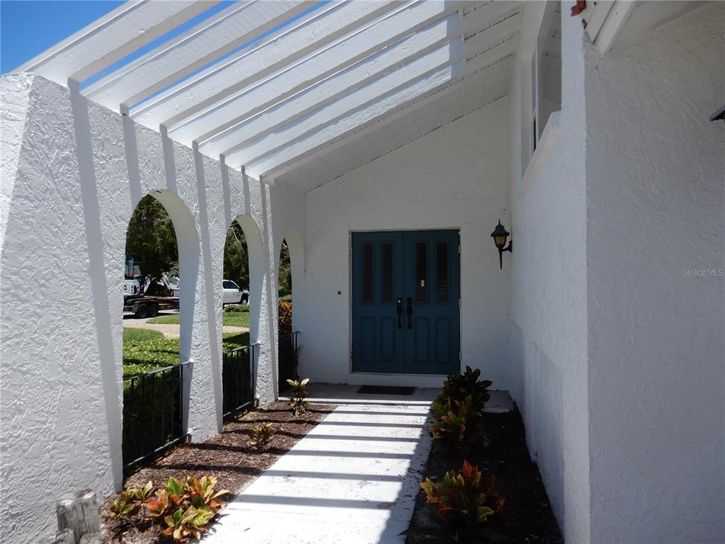 A white stucco house exterior features a covered entryway with arched openings and a pergola — 853 2ND AVENUE S, TIERRA VERDE, FL