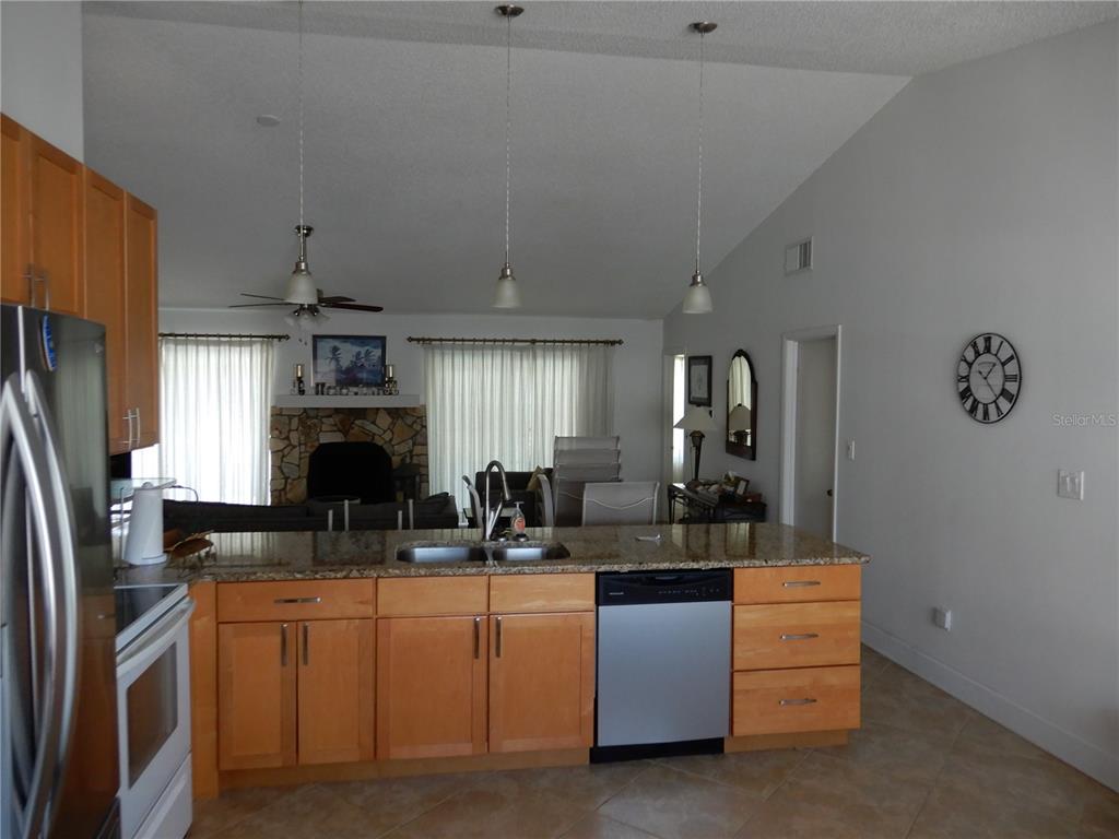A kitchen with light wood cabinets and granite countertops overlooks a living room with a fireplace — 853 2ND AVENUE S, TIERRA VERDE, FL