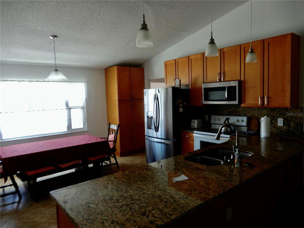 A kitchen with wood cabinets, granite countertops, stainless steel appliances, and an adjacent dining area — 853 2ND AVENUE S, TIERRA VERDE, FL
