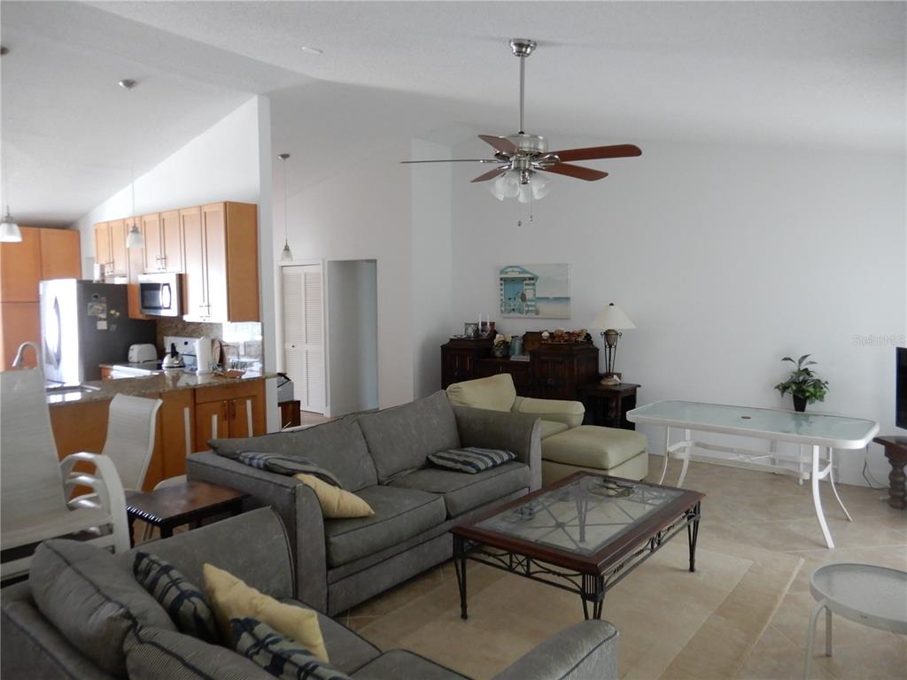 A living room with a gray sofa, glass coffee table, and an open-concept kitchen — 853 2ND AVENUE S, TIERRA VERDE, FL