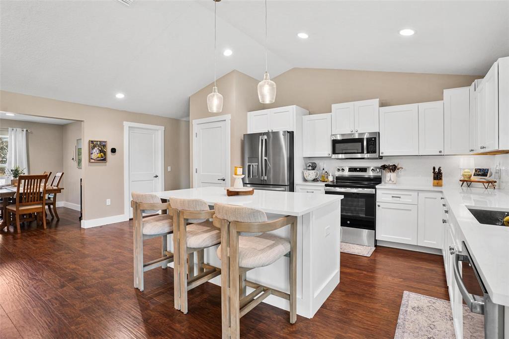A kitchen features white cabinets, a central island with bar stools, and dark wood flooring — 206 SHANNON LANE, LADY LAKE, FL
