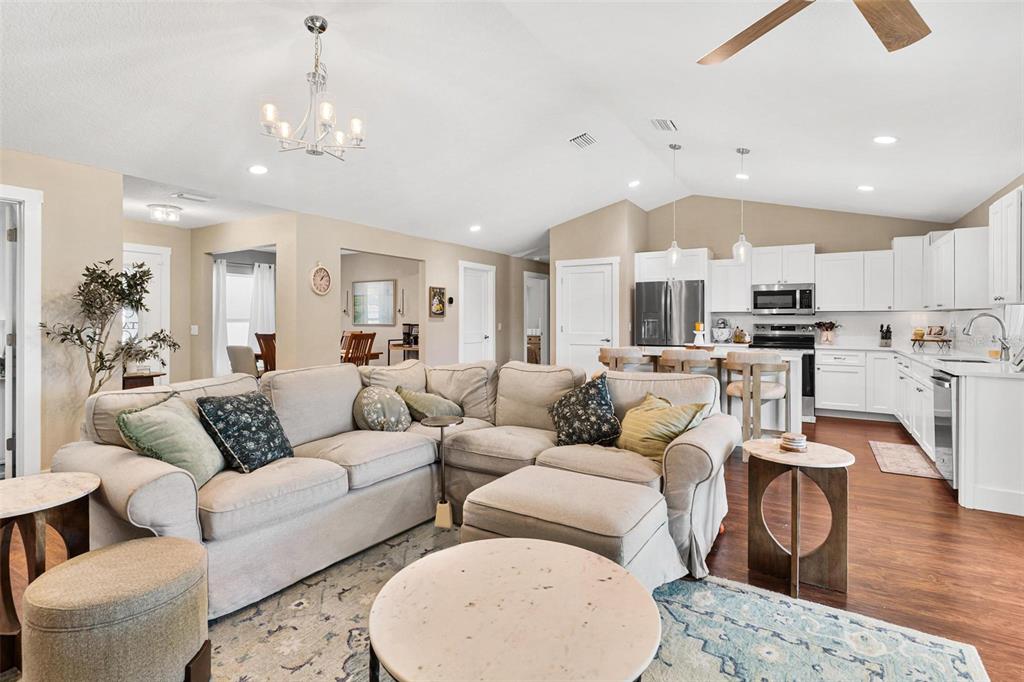 An open-concept living room features a large sectional sofa, a kitchen with white cabinets, and vaulted ceilings — 206 SHANNON LANE, LADY LAKE, FL