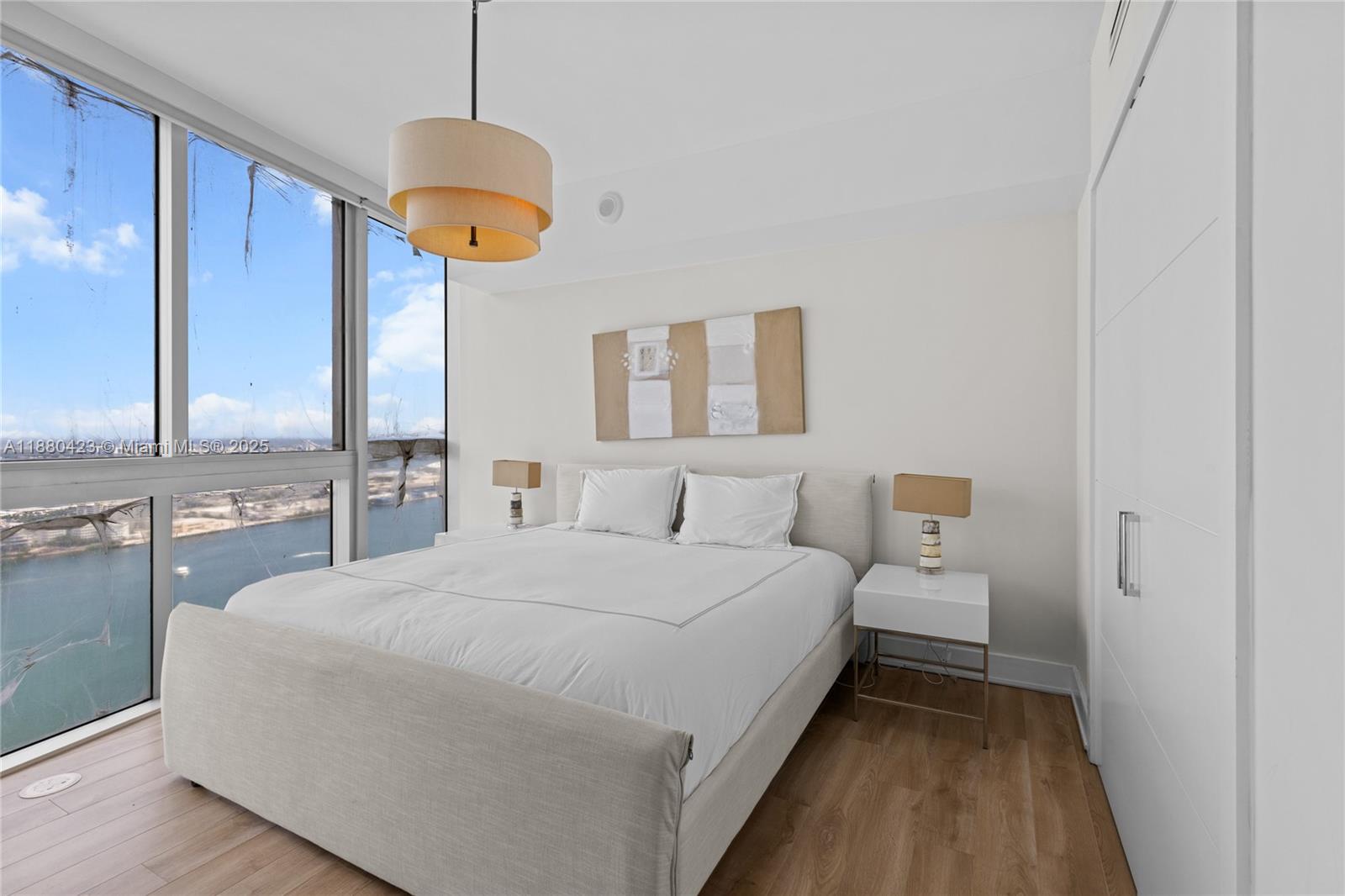 A bedroom features a bed, white nightstands, a hanging light fixture, and floor-to-ceiling windows — 465 Brickell Ave # 4901, Miami FL 33131, MIAMI, FL