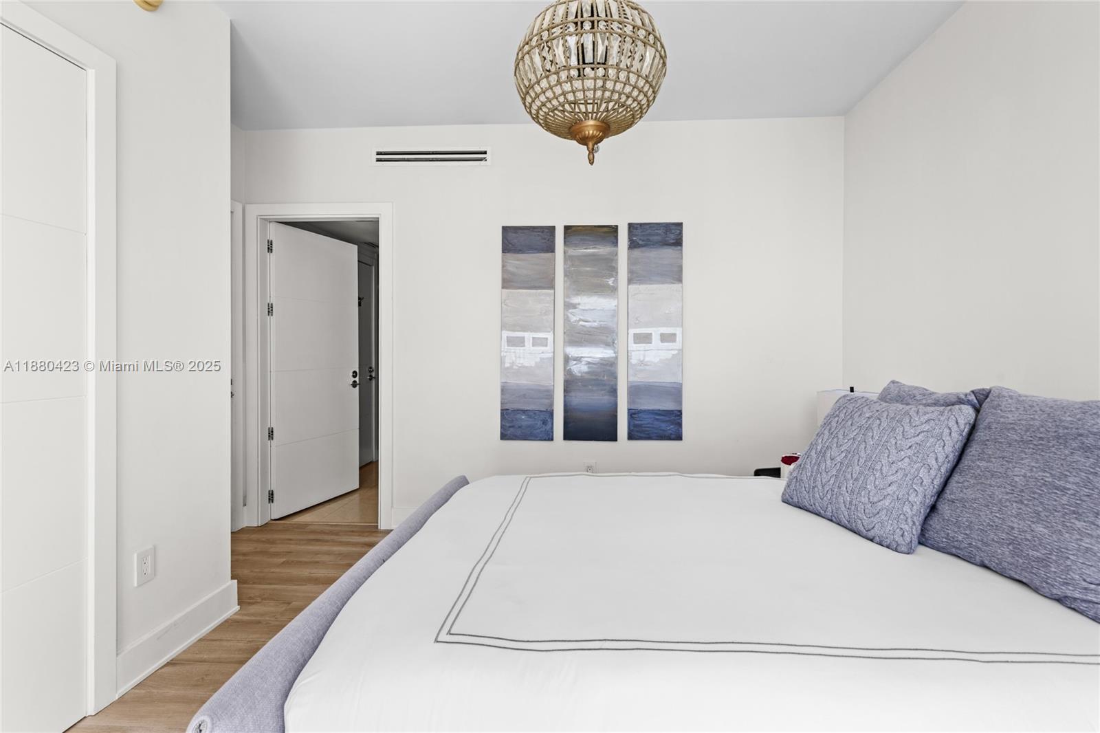 A bedroom features a bed with blue pillows, a chandelier, and three-panel wall art — 465 Brickell Ave # 4901, Miami FL 33131, MIAMI, FL