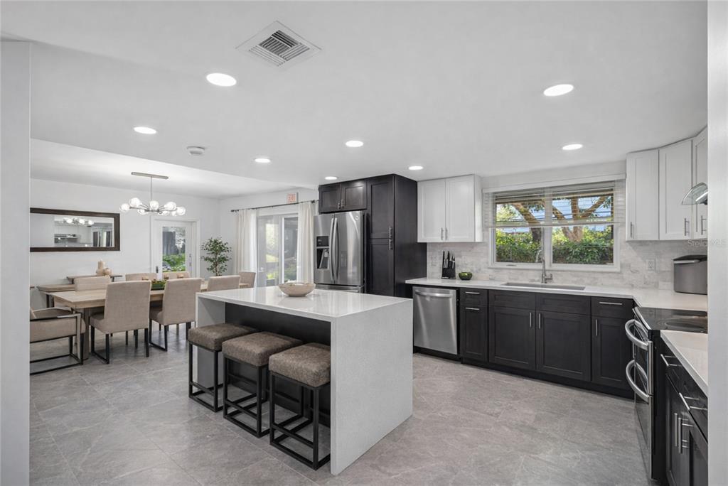 A modern kitchen features dark and white cabinetry, a quartz island, and an adjacent dining area — 10852 131ST STREET N, LARGO, FL
