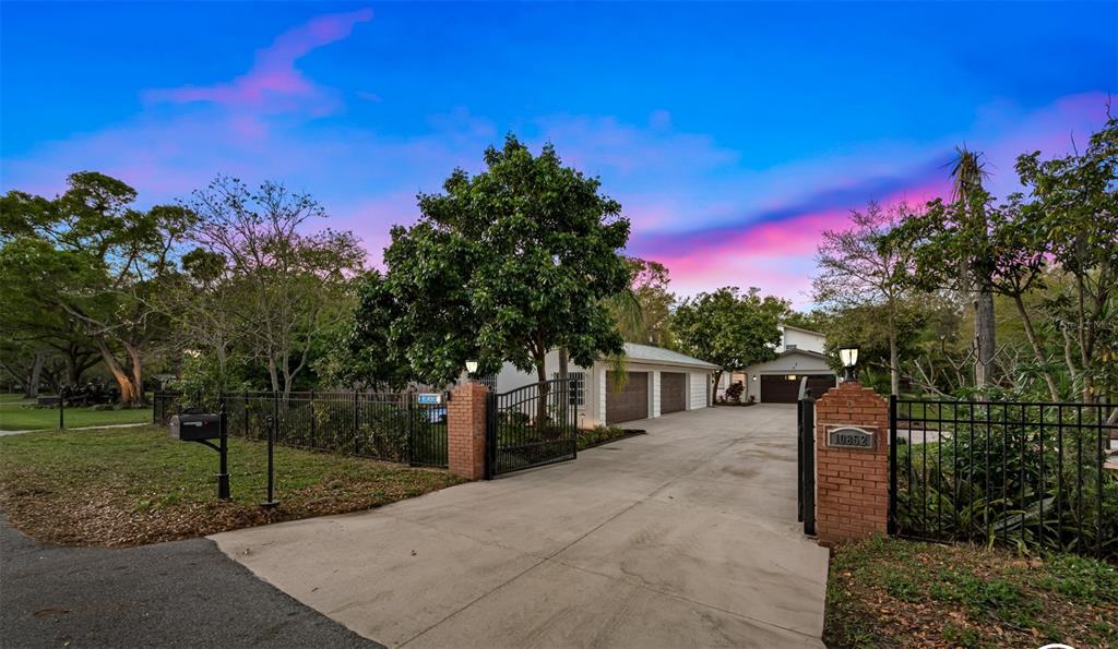 A concrete driveway leads to a house with a gated entrance and brick pillars — 10852 131ST STREET N, LARGO, FL