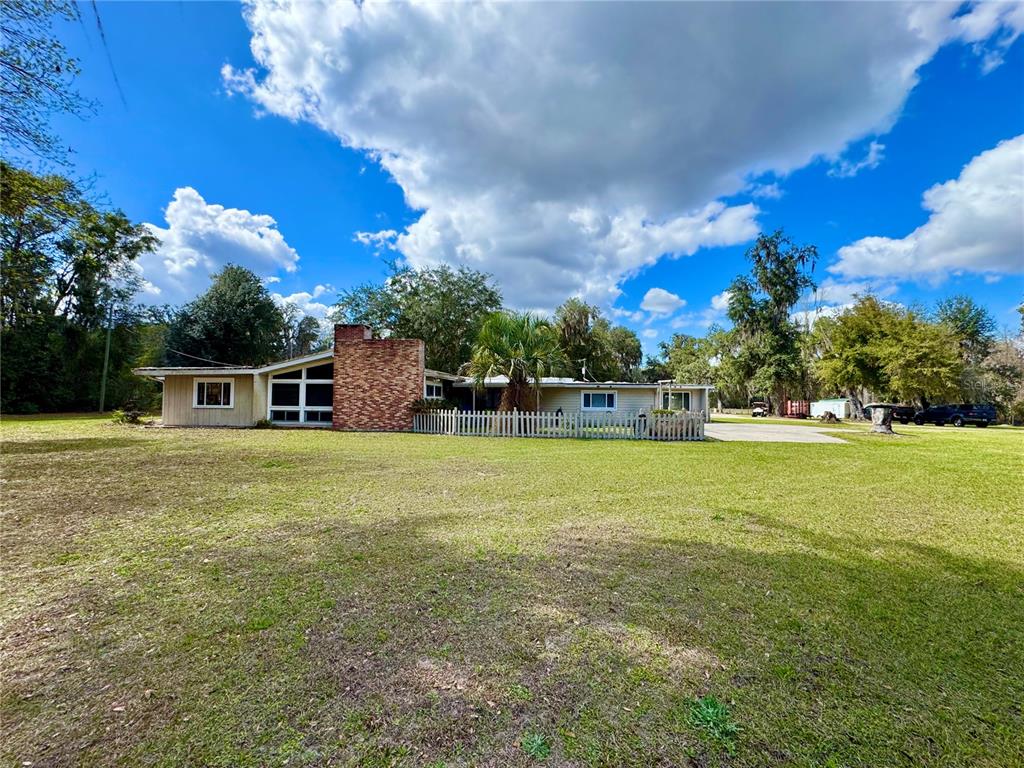 A single-story house with a brick chimney and a white fence sits on a lawn — 11816 SE COUNTY ROAD 234, MICANOPY, FL