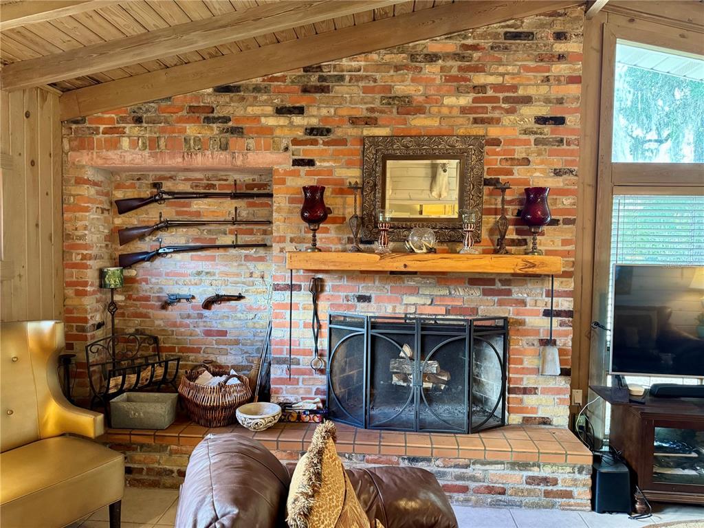 A brick fireplace with a wooden mantel and wall-mounted antique firearms in a living room — 11816 SE COUNTY ROAD 234, MICANOPY, FL