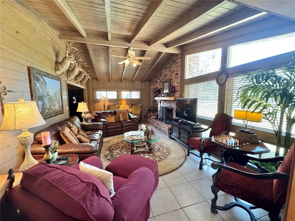 A rustic living room features wood-paneled walls, a vaulted ceiling, a brick fireplace, and tile flooring — 11816 SE COUNTY ROAD 234, MICANOPY, FL