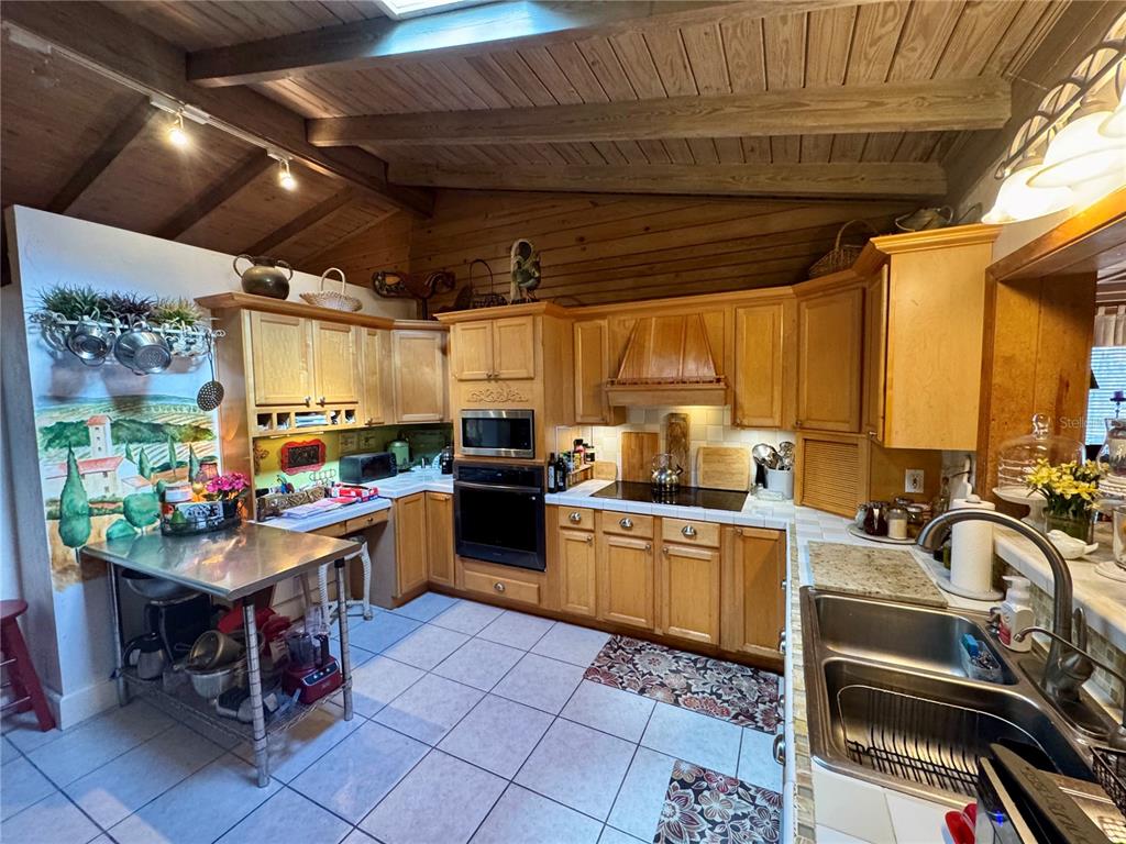 A kitchen with wood cabinets, stainless steel appliances, tile flooring, and a vaulted wood ceiling — 11816 SE COUNTY ROAD 234, MICANOPY, FL