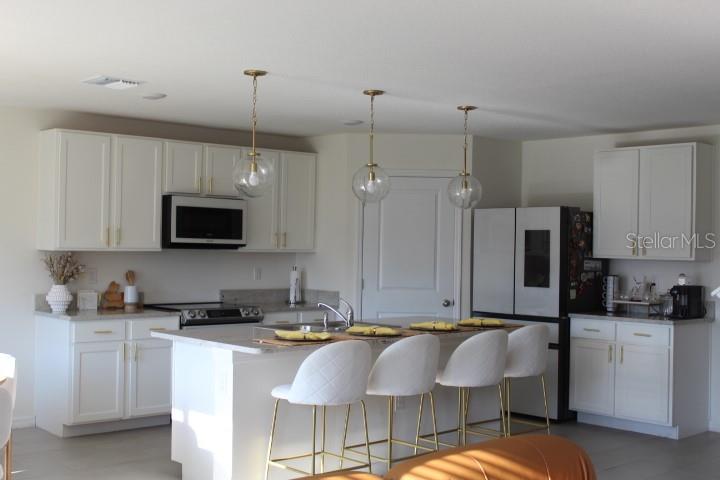 A modern kitchen features white cabinets, a central island with bar seating, and pendant lighting — 2182 NW 246TH TERRACE, NEWBERRY, FL